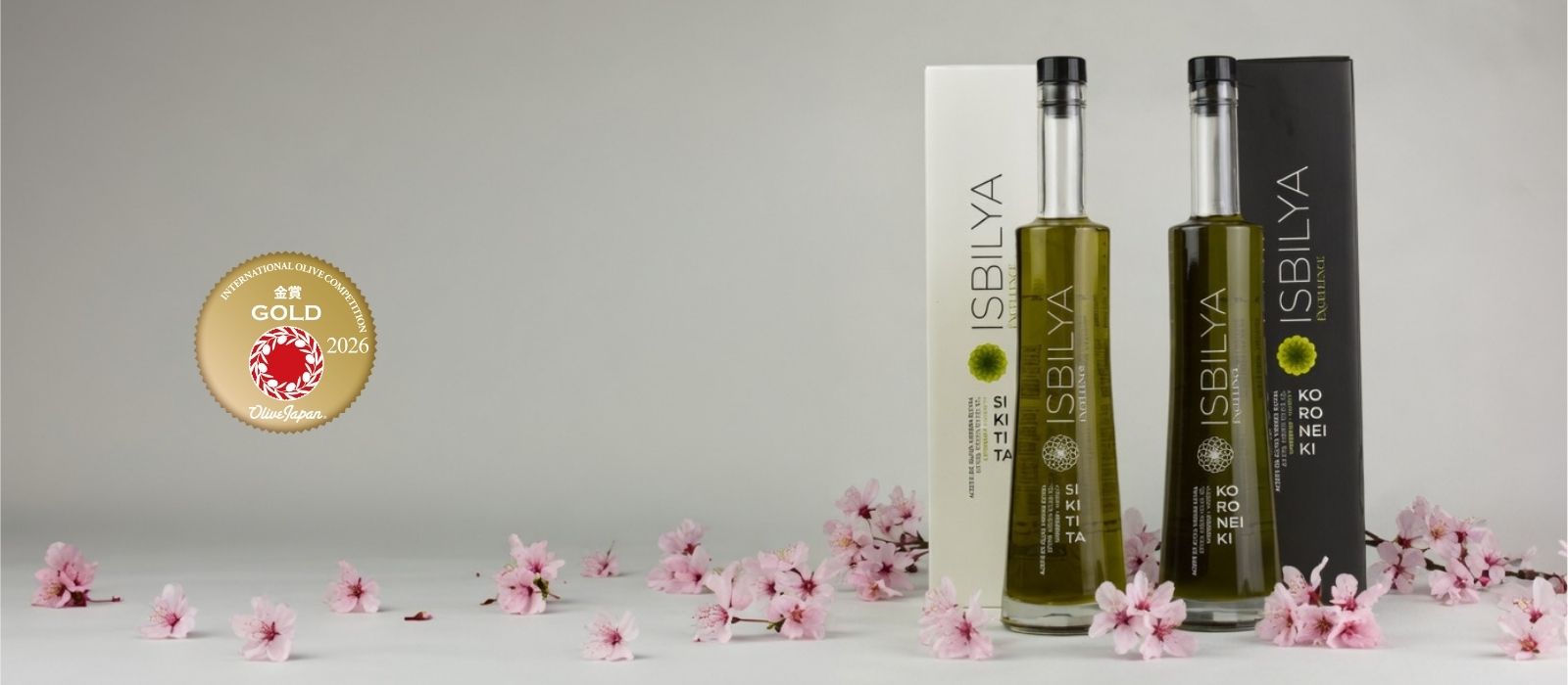 Botellas y estuches de isbilya sikitita y koroneiki sobre flores de cereza y el logo que acredita la medalla de oro en el concurso internacional de aceite de oliva de Japón.