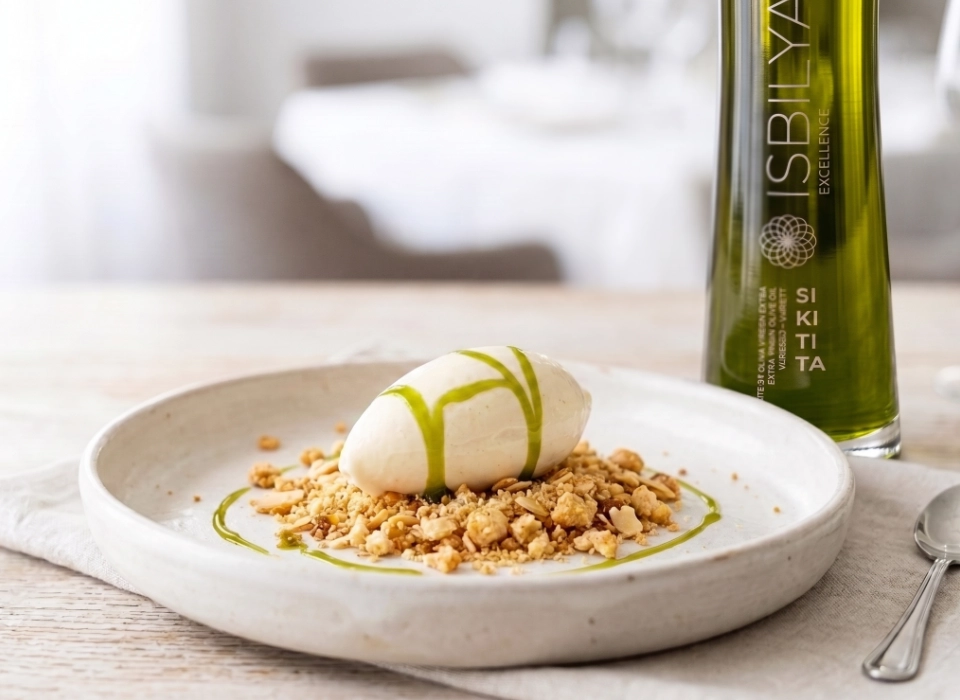 Helado de aceite de oliva virgen extra cremoso sobre una base crujiente de crumble rústico de almendras enteras en un plato de alta cocina con botella de AOVE Isbilya Sikitita
