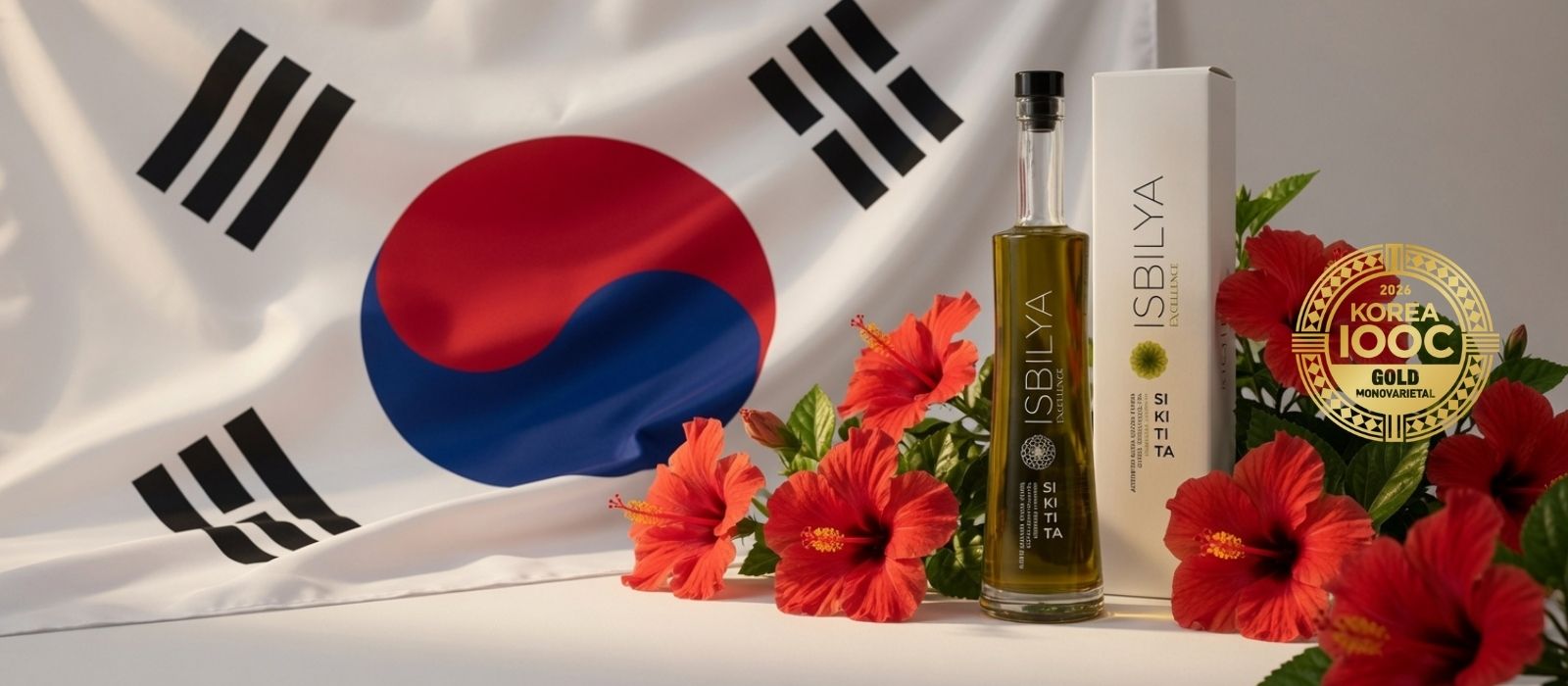 Botella y estuche de aceite de oliva Isbilya Sikitita junto a flores de hibisco rojas con la bandera de Corea del Sur de fondo, premio internacional.