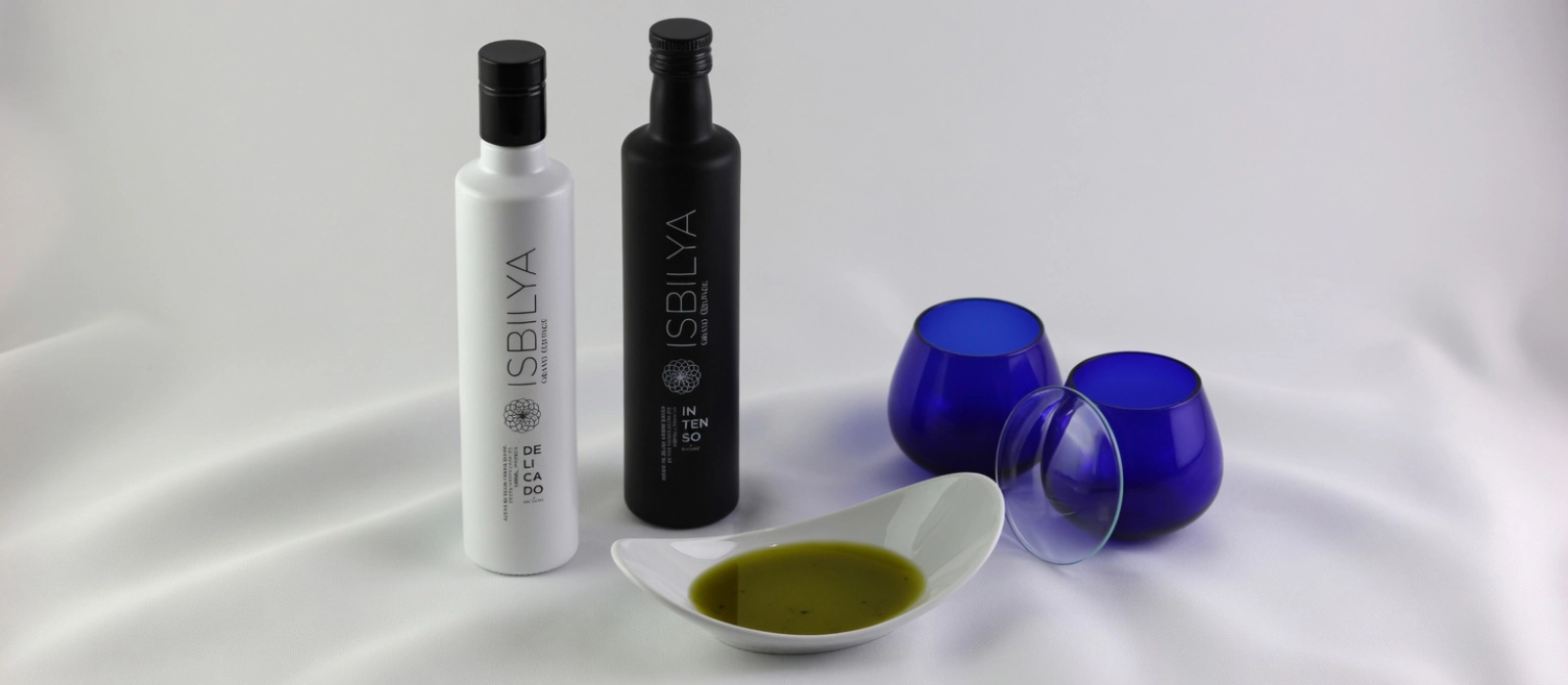 Coupage, el arte de ensamblar AOVEs | Isbilya Botellas de Grand Coupage Delicado e Intenso con vasos de cata de AOVE y plato con aceite de oliva virgen extra.